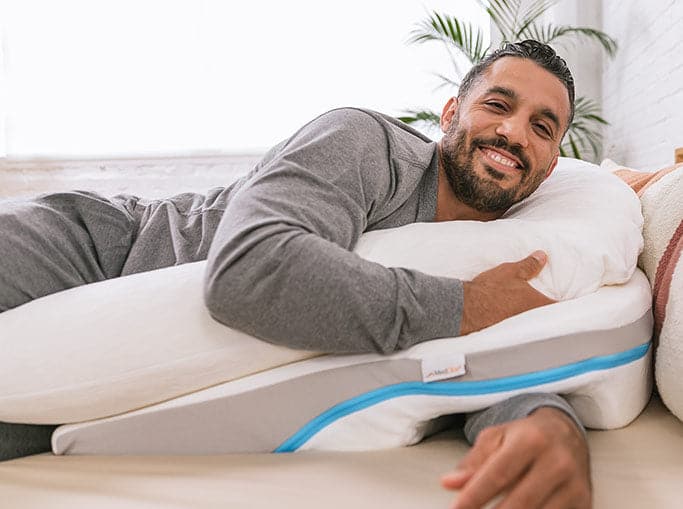 A smiling man laying on the MedCline Shoulder Pain Relief Pillow