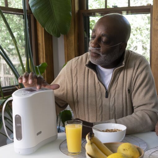 A man presses the Oxlife LIBERTY™ Portable Oxygen Concentrator buttons whilst sitting at the breakfast table