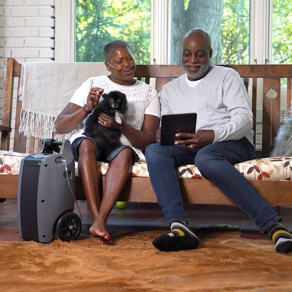 A couple sitting on a bench. The woman is using the Oxlife Independence Portable Oxygen Concentrator
