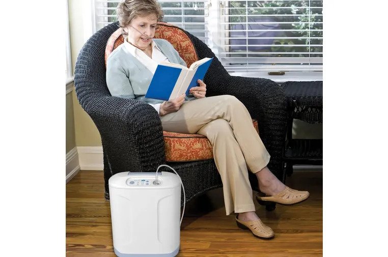 A women reading a book while using the Inogen At Home Stationary Oxygen Concentrator