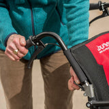 An older woman holding the handle of the Journey So Lite Wheelchair and releasing the wheelchair lock with another hand.