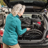 An older woman putting a folded Journey So Lite Wheelchair into a car trunk