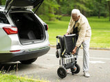 An older person folds up the Journey Zoomer® Folding Power Chair next to a car’s open trunk